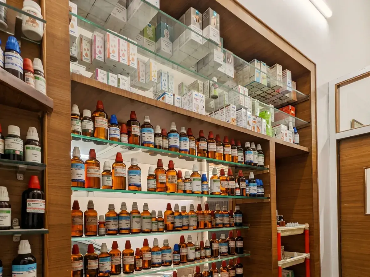 Shelves stocked with amber homoeopathic remedy bottles at the clinic pharmacy